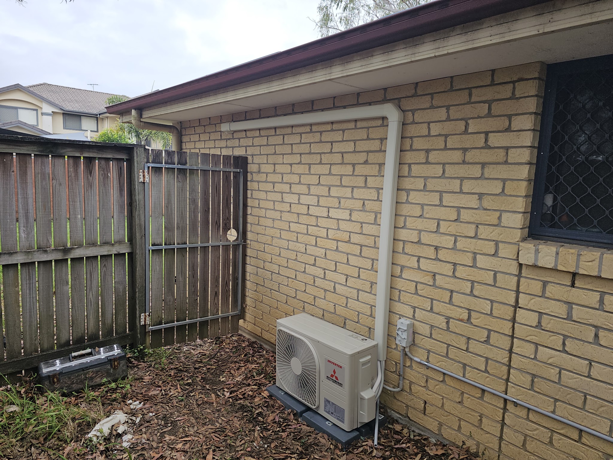 Outdoor air conditioning unit installed against a brick home beside a timber fence