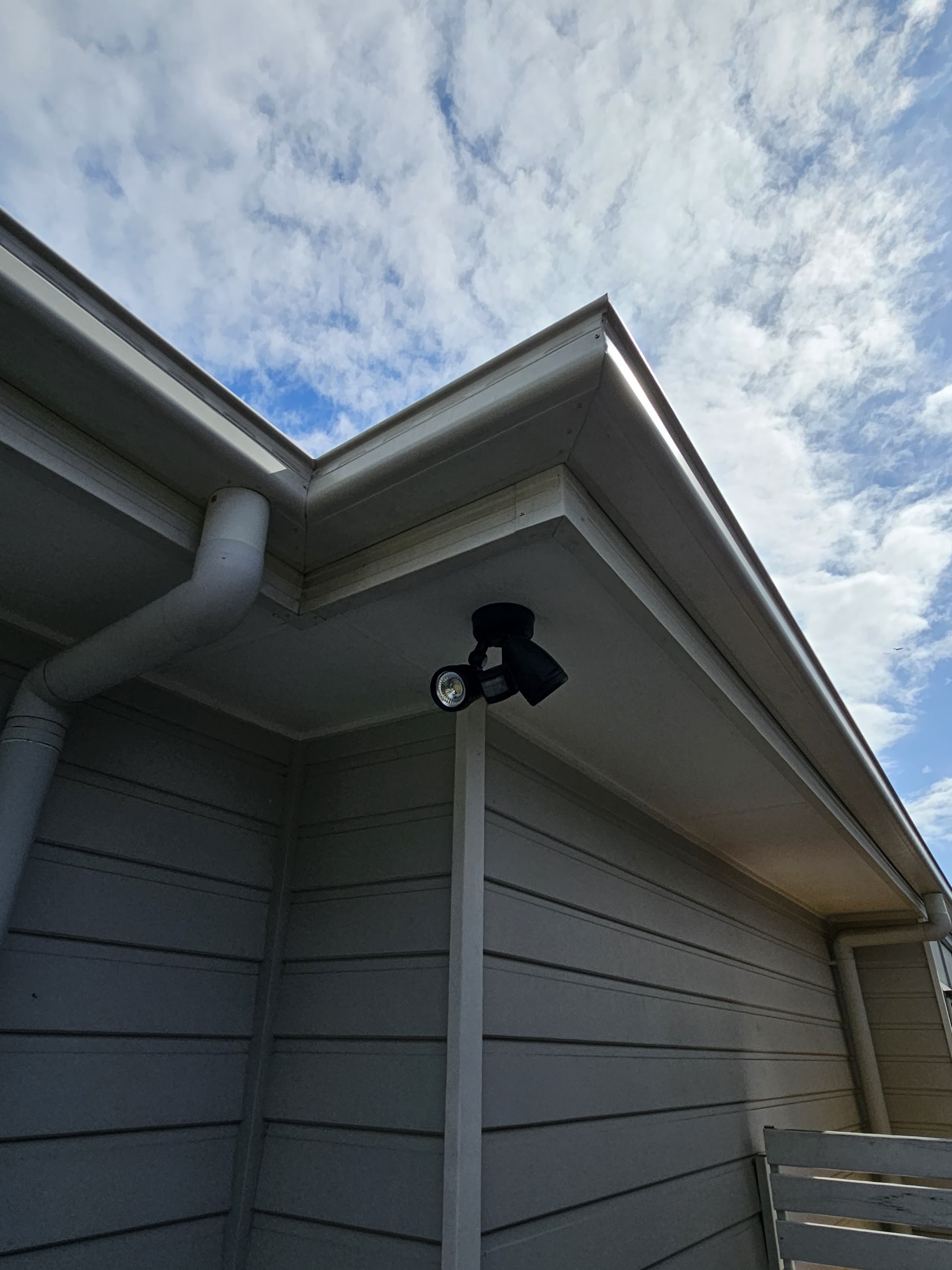 Sensor floodlight mounted under the eave of a house against a blue sky