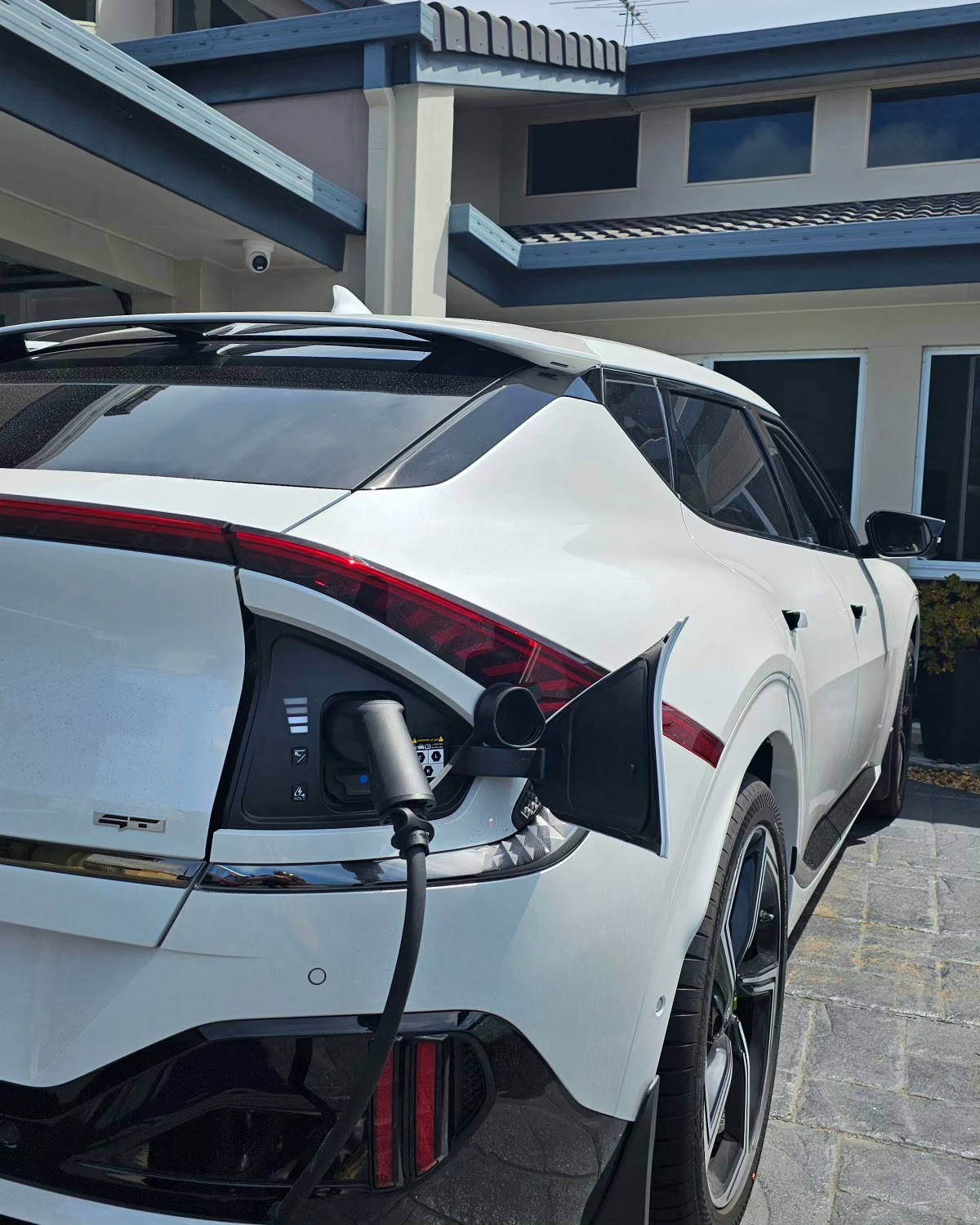 White electric car plugged into a home charger in a paved driveway