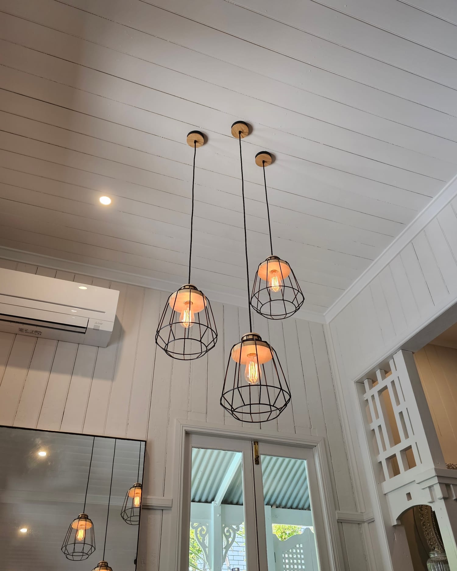 Three caged pendant lights hanging from a high timber-lined ceiling in a Queenslander-style home