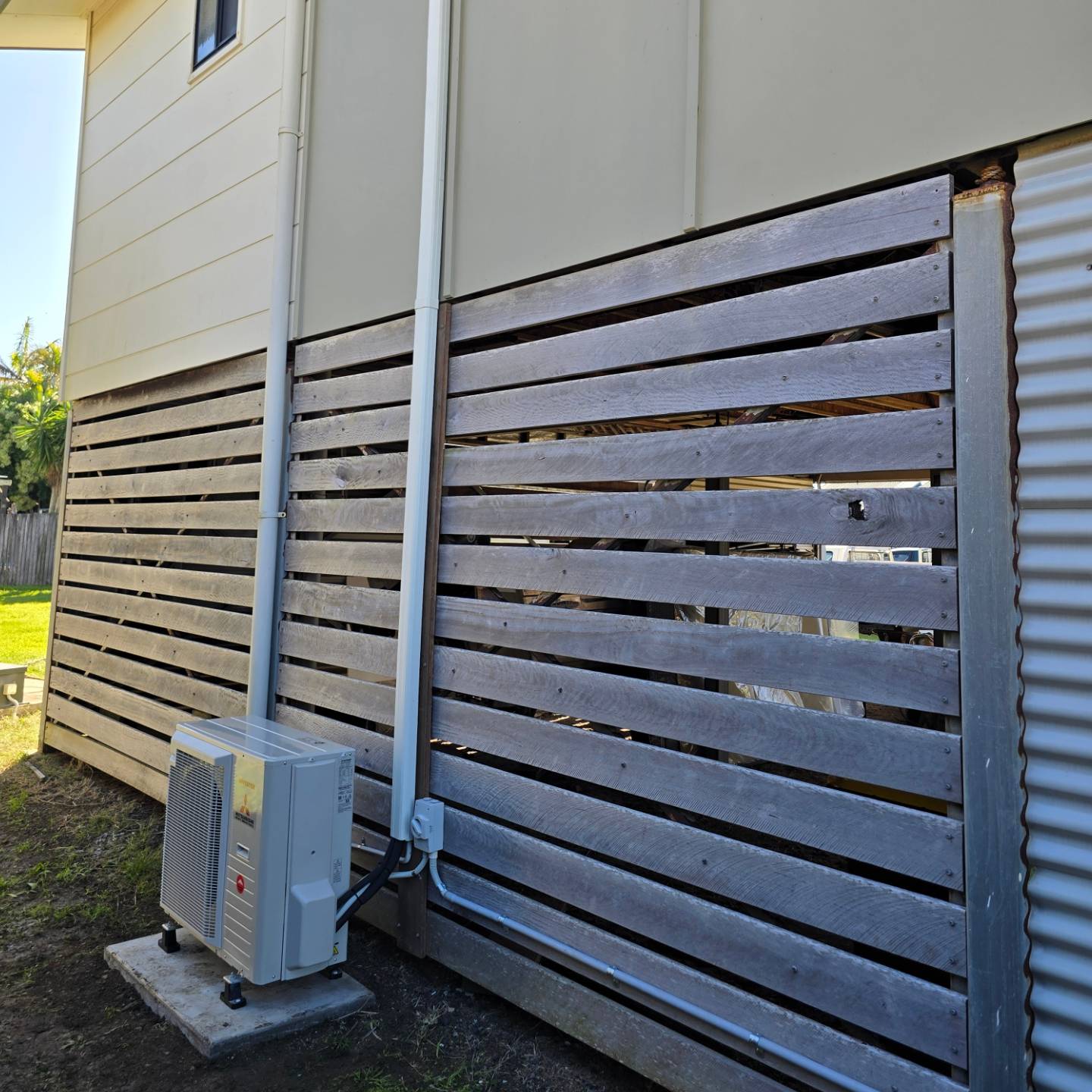 Outdoor air conditioning unit at the base of a high-set home with timber slat screening